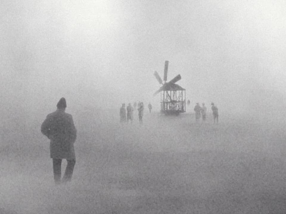 Menschen stehen im Nebel um eine Windmühle herum.
