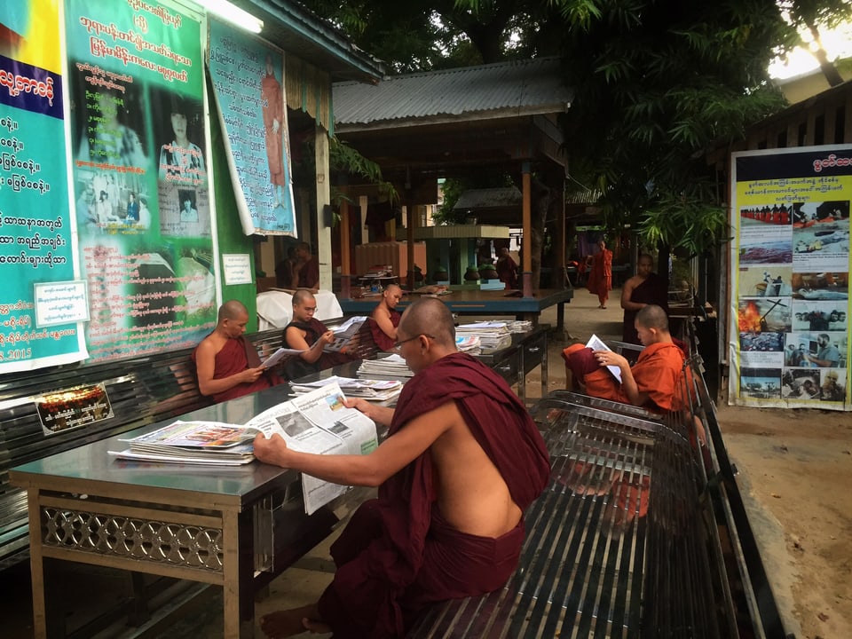 Mönche in einem buddhistischen Kloster in Burma. Sie sitzen am Tisch und lesen Zeitung. 