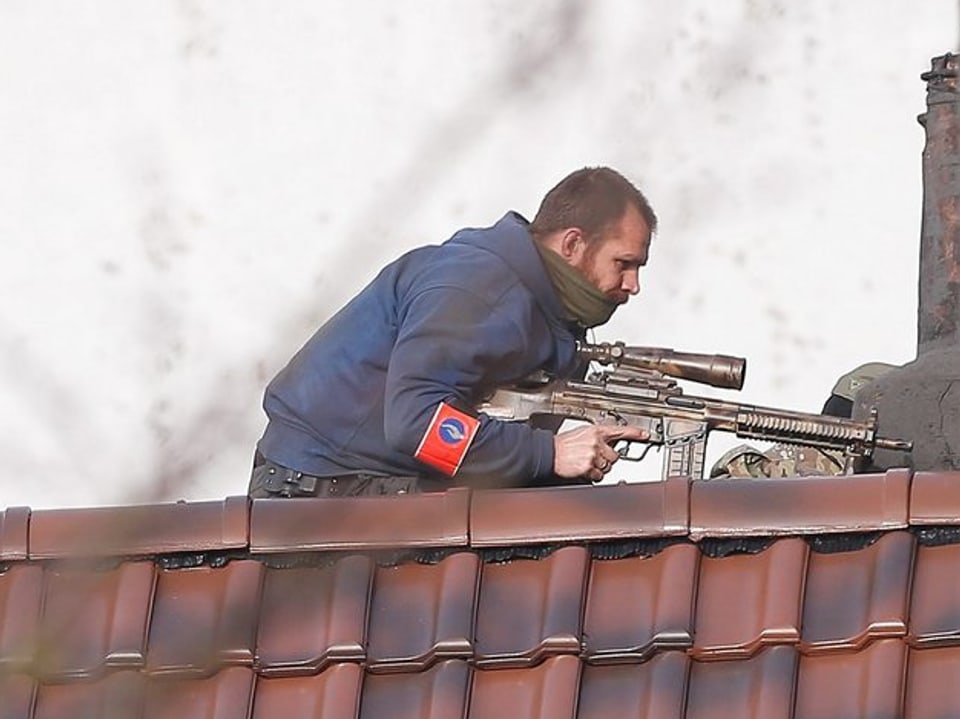 Ein bewaffneter Polizeibeamter positioniert sich auf einem Dach 