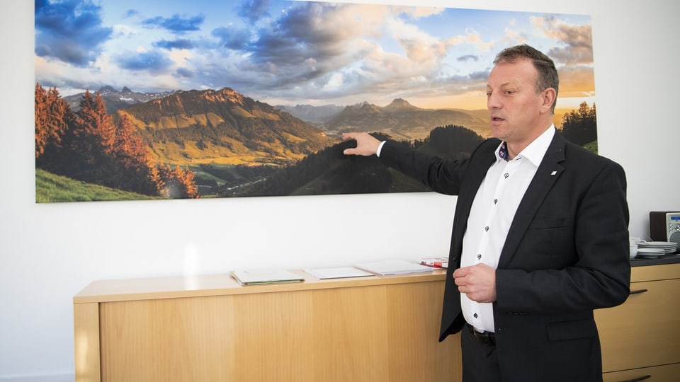 Didier Castella zeigt mit der rechten Hand auf ein Bild von Bergen