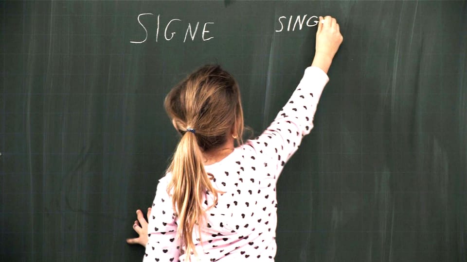 Ein Kind schreibt mit Kreide an die Tafel das Wort «Signe».