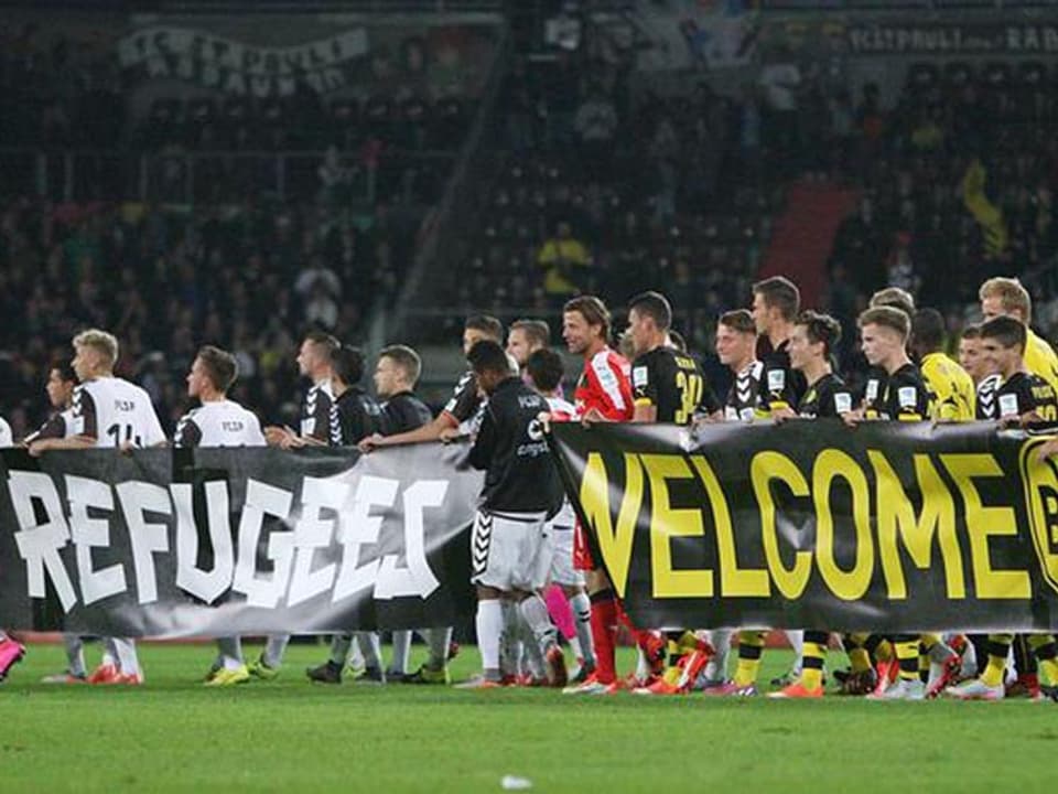 Ein grosses Banner wird von den Spielern getragen. Darauf steht: Refugee are welcome.