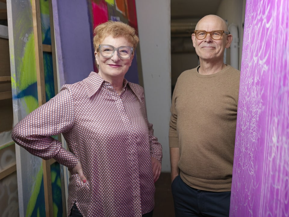 Mann und Frau posieren lächelnd zwischen bunten Gemälden.