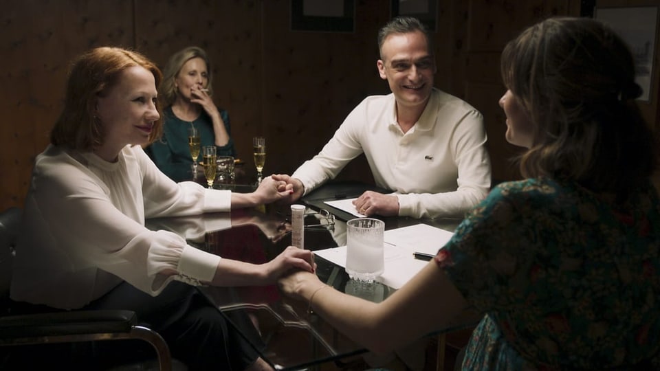 Vier Menschen sitzen an einem Tisch und halten Händchen