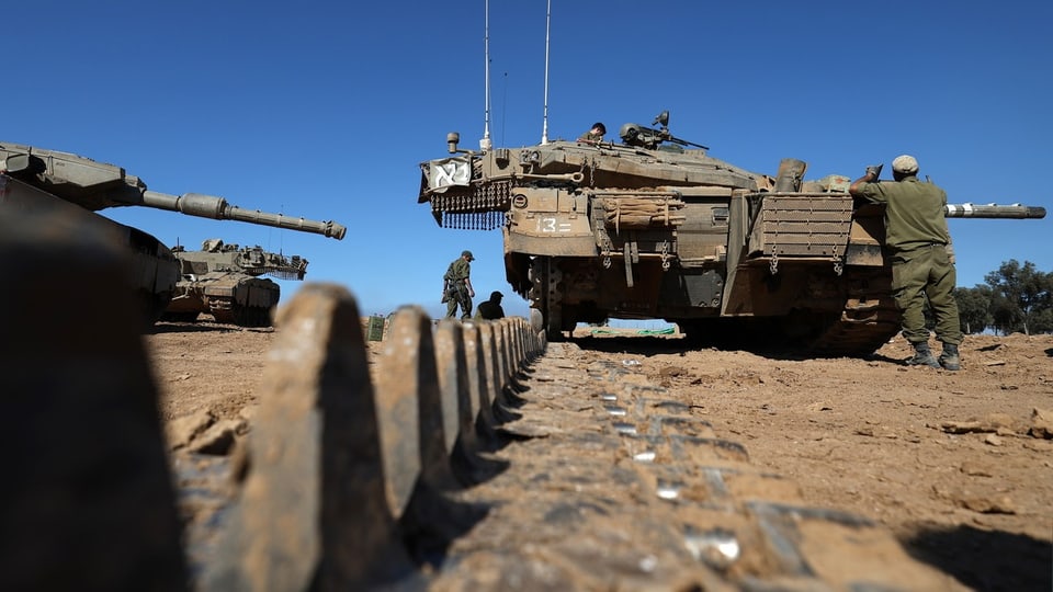 Ein Panzer mit einem Soldat davor, im Vordergrund Bodenschranken, links weitere Panzer