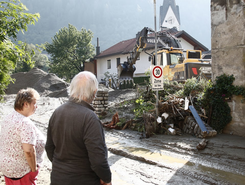 Zwei ältere Personen schauen den Aufräumarbeiten im Dorf zu.