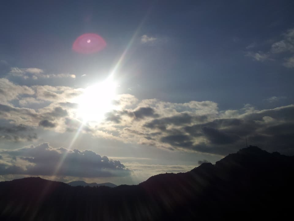 Im Vordergrund im Schatten der Hügelzug des San Salvatores, inklusive Antenne. Darüber trotz Wolkenfelder ein meist blauer Himmel.