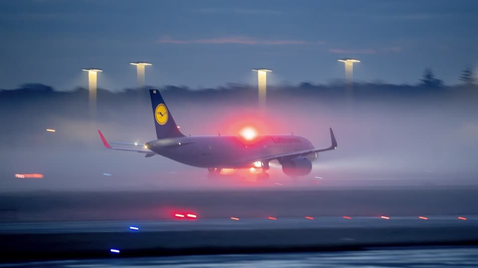 Ein Lufthansa-Flugzeug fährt auf einer Landebahn. Rotes Licht leuchtet über dem Flugkörper.