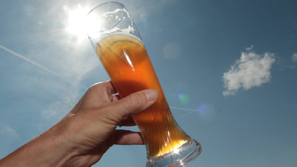 Eine Hand hält ein Glas Weissbier gegen die Sonne