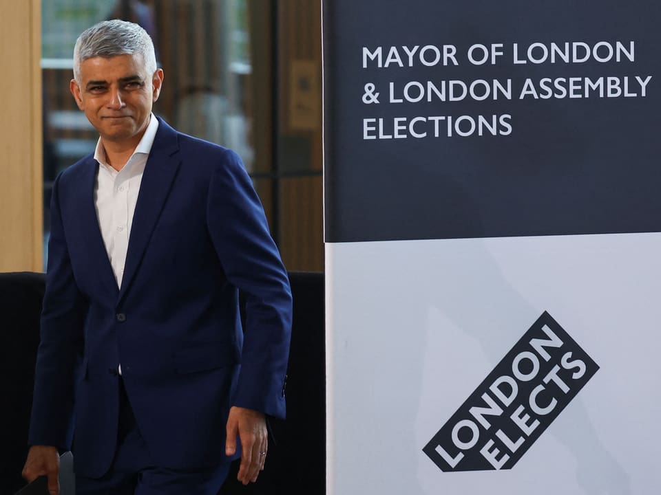 Mann in blauem Anzug steht neben Banner zur Bürgermeister- und Parlamentswahl in London.