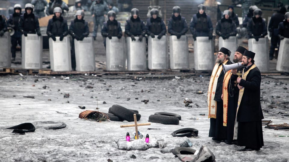 Priester, im Hintergrund Polizisten, während der Ausschreitungen in Kiew im vergangenen Februar.