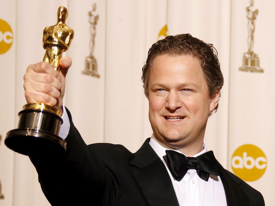 Ein Mann im Smoking hält stolz eine goldene Oscar-Statue in der Hand.