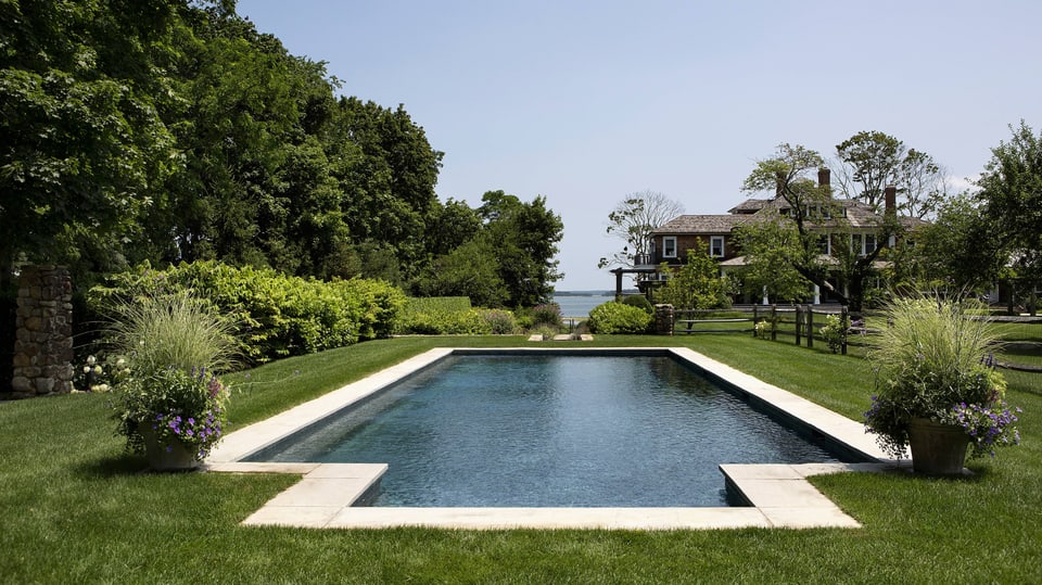Ansicht eines Pools in einem Garten bei Sonnenschein in den Hamptons. In den Hintergrund das Haus und der Horizont.