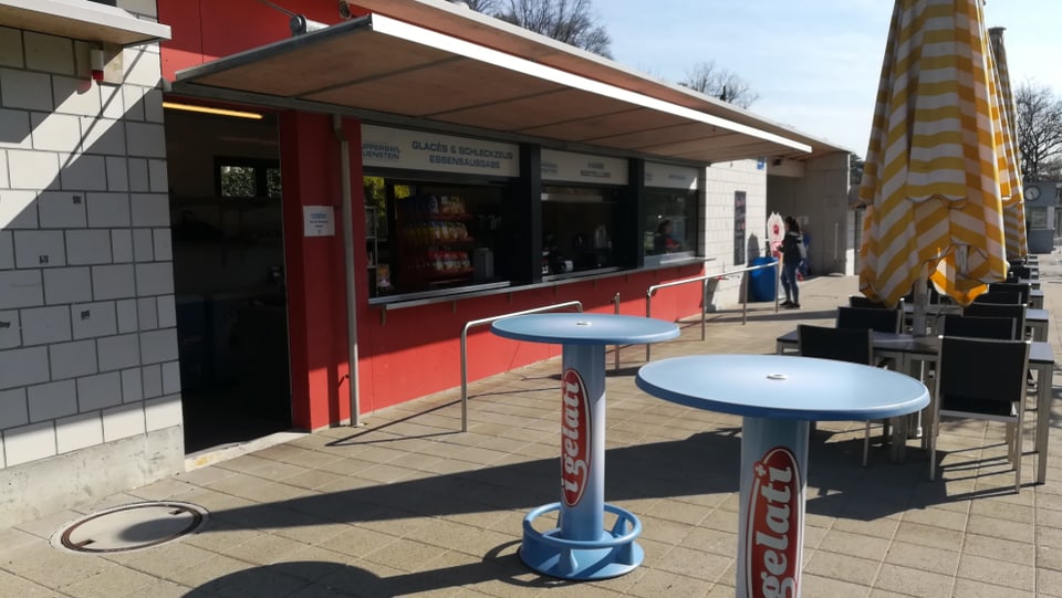 Kiosk mit Tischen, Stühlen und Sonnenschirmen.