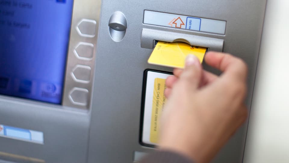 Eine Frau steckt ihr Postfinance-Kärtchen in einen Postomat. (keystone)