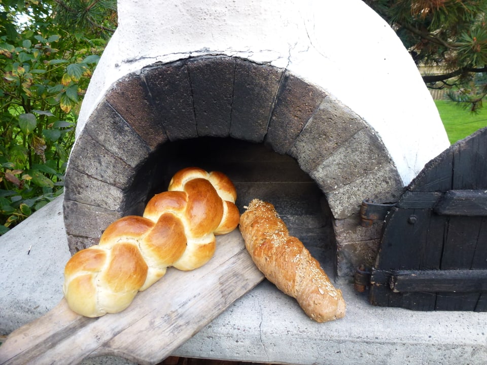 Zopf und Brot liegen auf einer Holzschaufel beim Holzofen.