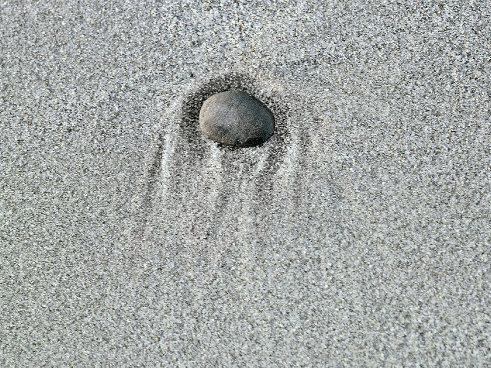 Ein grauer Stein in feinem grauen Sand.