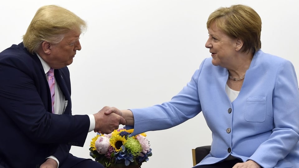 Trump - links in schwarzem Anzug - und Merkel - rechts im hellblauen Blazer - schütteln sich sitzend die Hand.