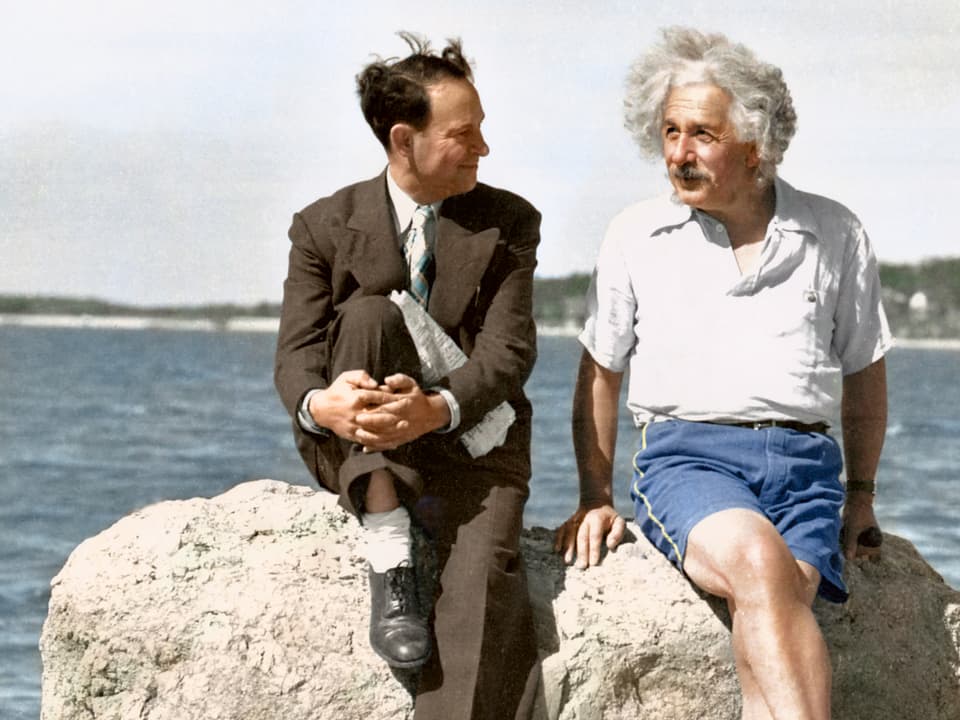 Zwei Männer sitzen auf einem Stein und sprechen miteinander