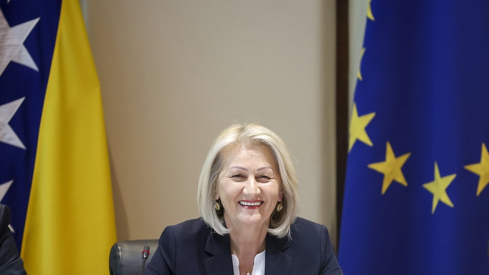 Eine blonde Frau zwischen der EU-Fahne und der Fahne von Bosnien-Herzegowina