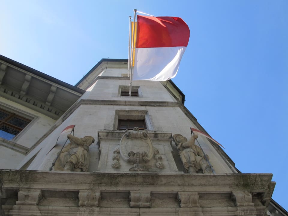 Bild vom Treppenturm des Solothurner Rathauses, aufgenommen von unten mit Blick der Wand entlang in den Himmel hinauf. Vor einem der Fenster hängt eine Solothurner-Fahne.