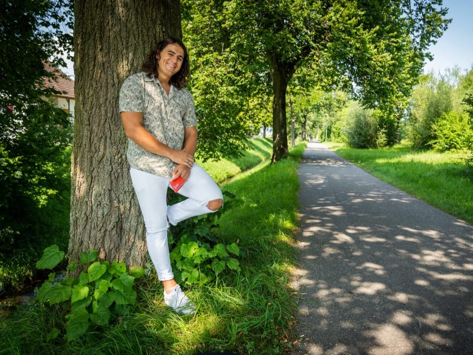 Mann mit rotem Schweizerpass in der Hand lehnt an einen Baum in der Natur