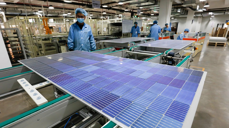 Arbeiter in chinesischer Firma steht vor Solarpanel