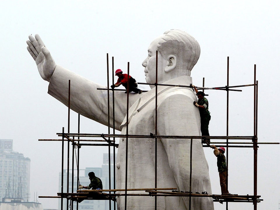 Bauarbeiter auf einen Gerüst, das an einer gigantischen Mao-Statue befestigt ist.