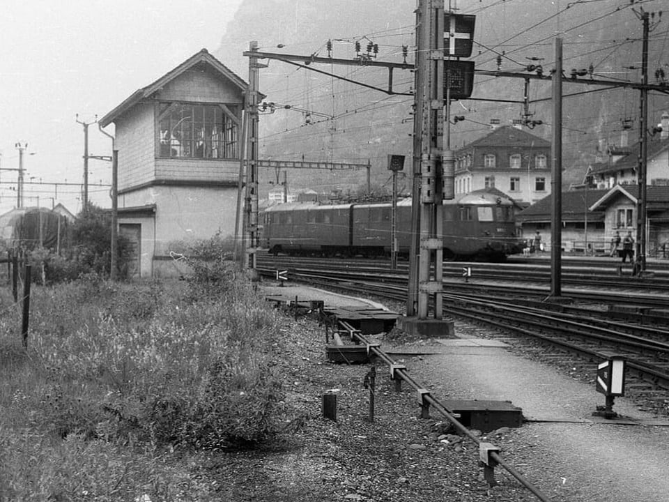 Bahnhof Erstfeld mit Zug und einem kleinen Haus mit Giebeldach.