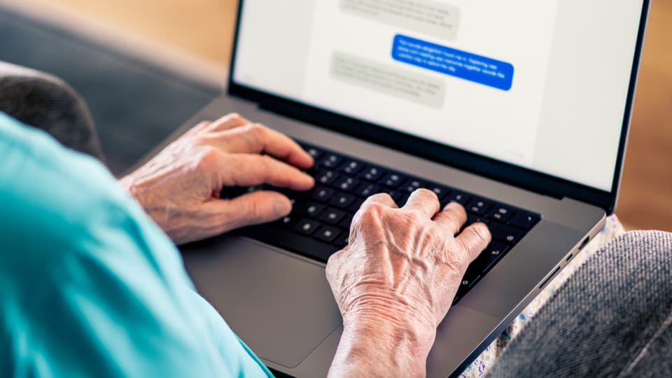 Die Hände einer älteren Frau schreiben auf einem Laptop in einem Chat-Programm