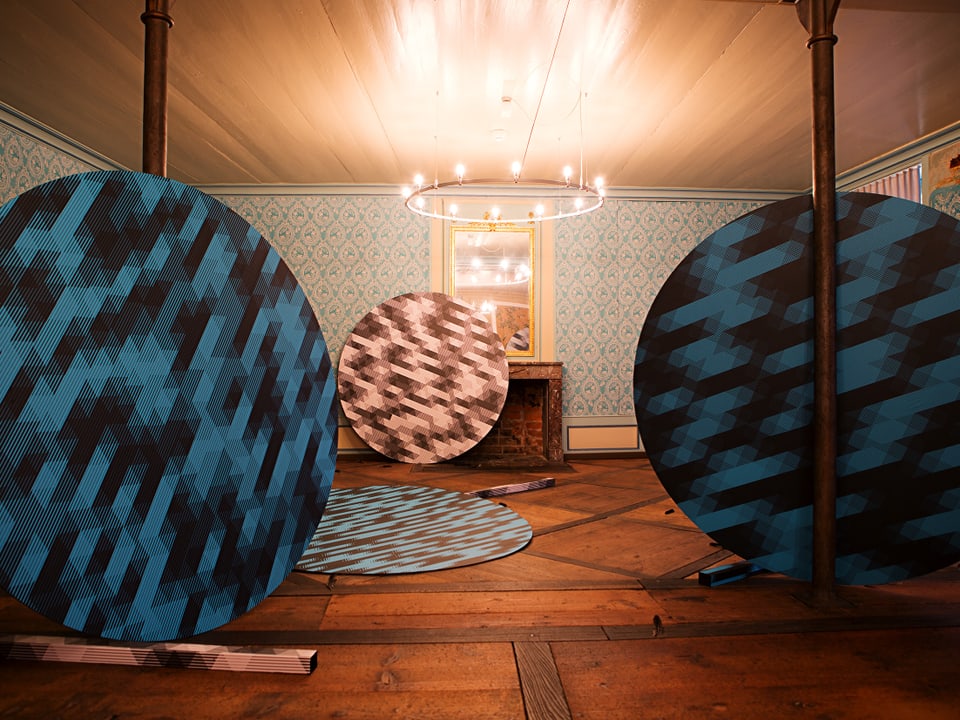 Runde, farbige Platten stehen angelehnt herum in einem Raum mit Tapeten.