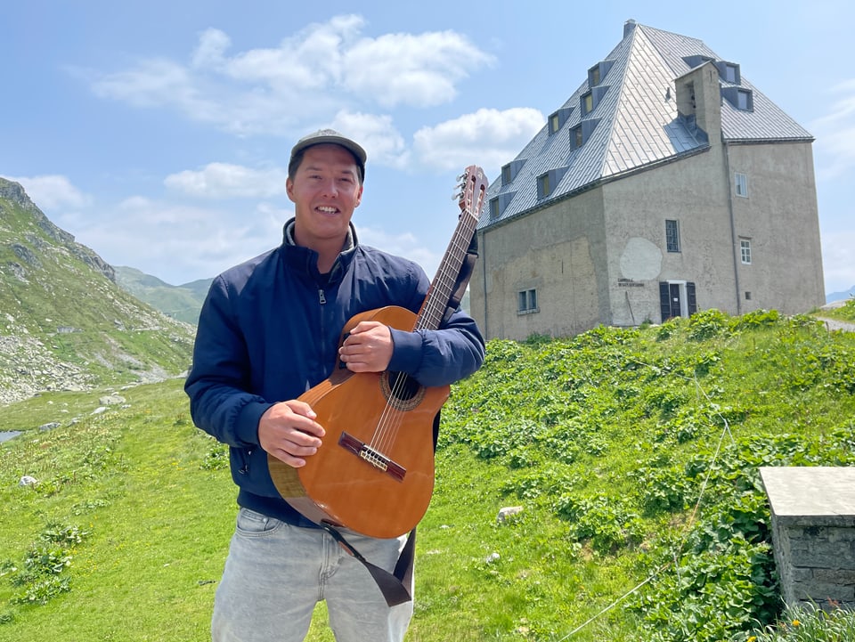 Mattiu sitz auf einem Stuhl mit einer Gitarre auf dem Schoss und schaut in die Kamera. 