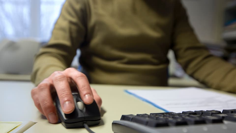 Mann sitzt an Computer, Maus in der Hand