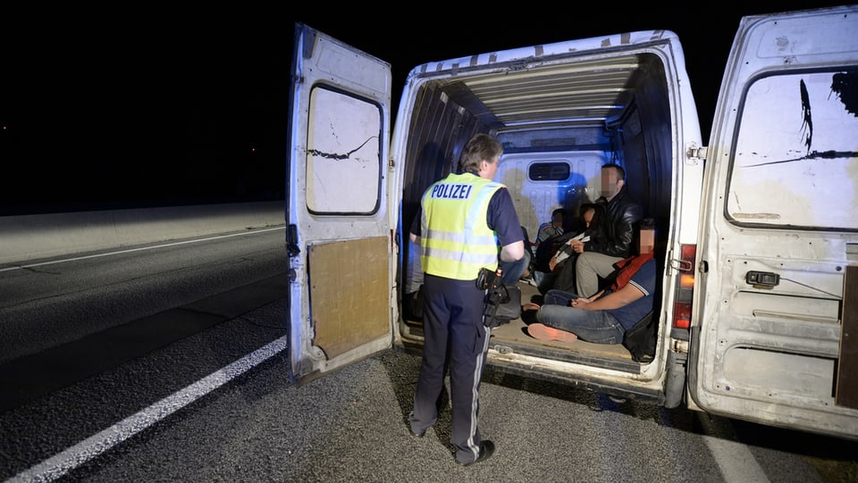 Ein Polizist steht vor einem Lieferwagen mit Migranten drin. 