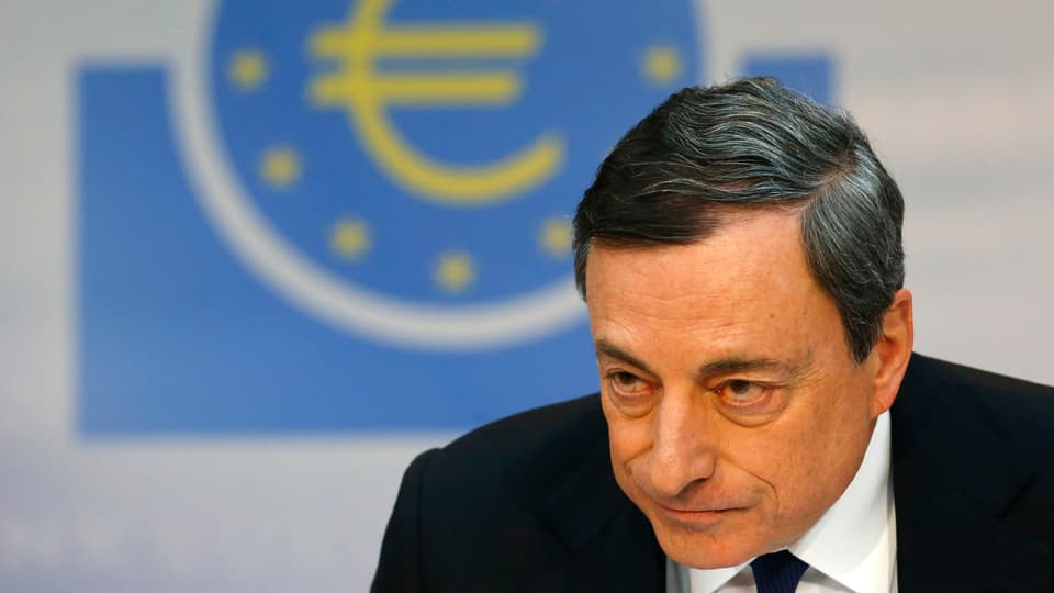 Mario Draghi dahinter das Euro-Symbol an der Wand.