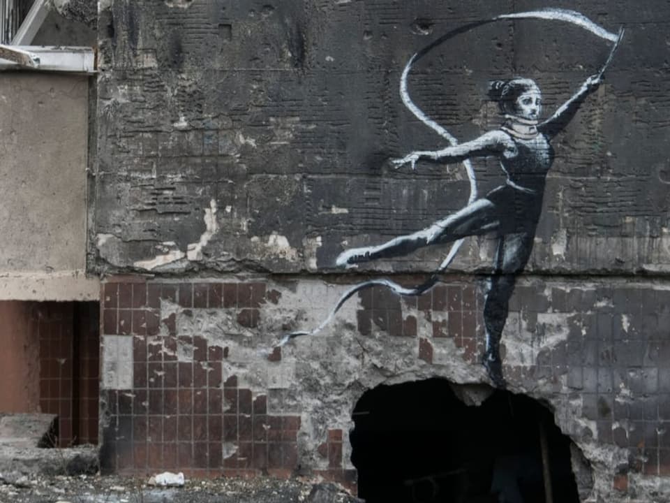 Graue Wand, darauf in schwarzweiss eine junge Frau, schwingt mit erhobenem Arm ein Band.