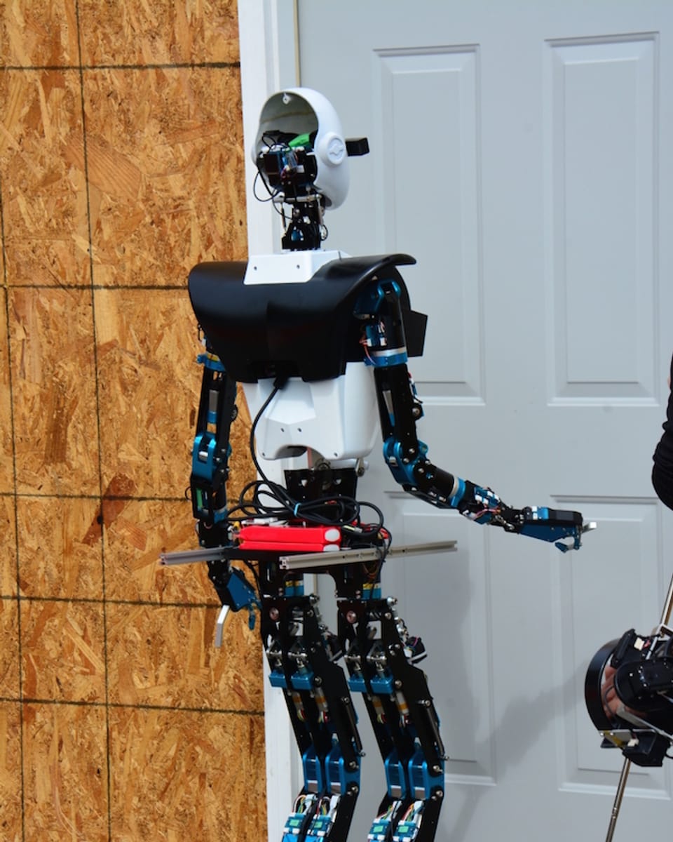 Ein humanoider Roboter mit Armen und Beinen steht vor einer Tür.
