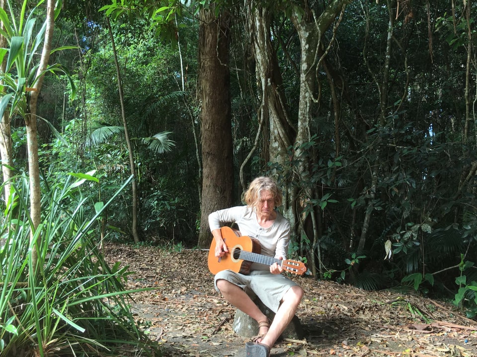 Jogl sitzt mit Gitarre im Regenwald.