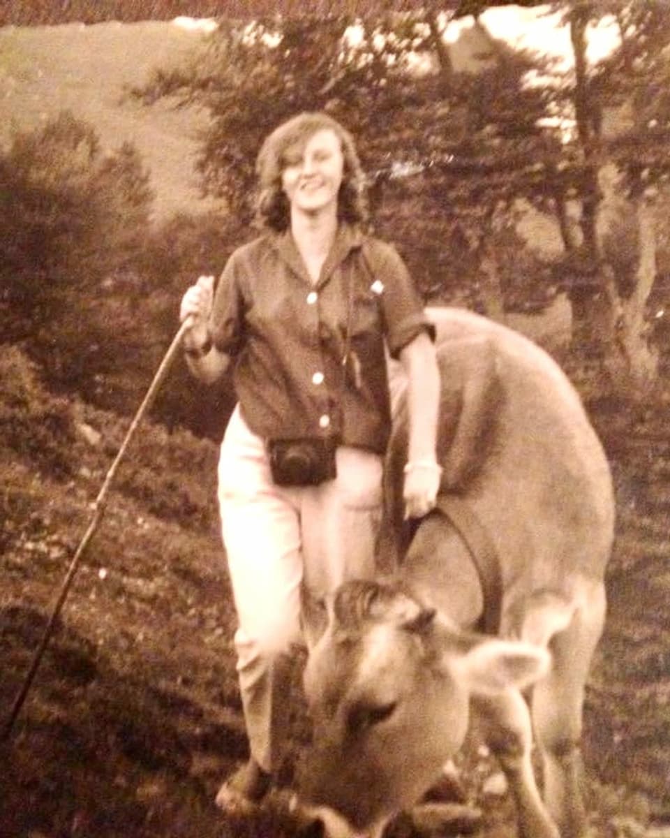 Eine Frau mit Stock steht neben einer Kuh im Jahr 1960.