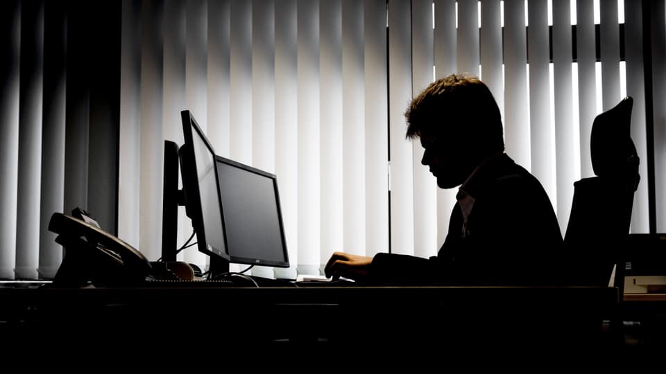 Symbolbild: Mann im Gegenlicht vor einem Computer.