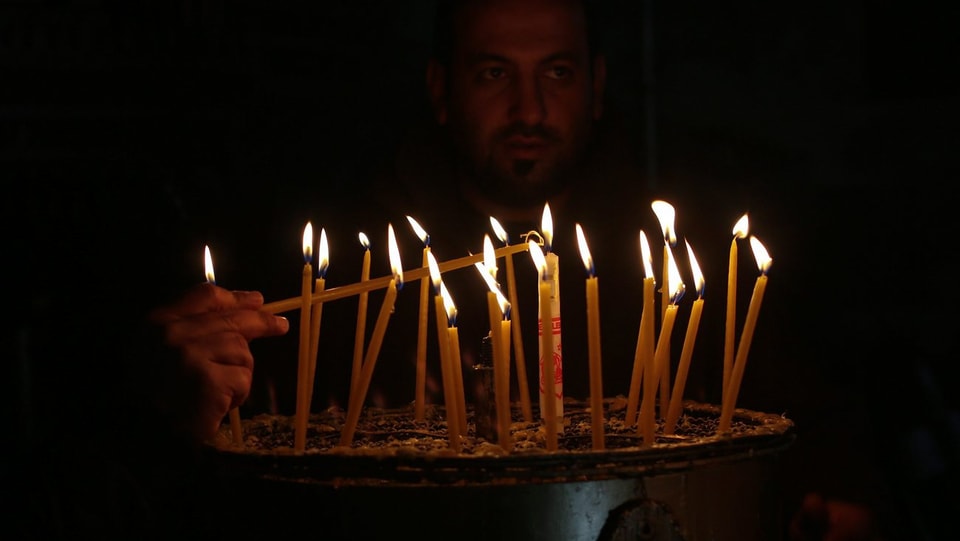 Ein Pilger entflammt kleine Kerzen in der dunklen Kirche.