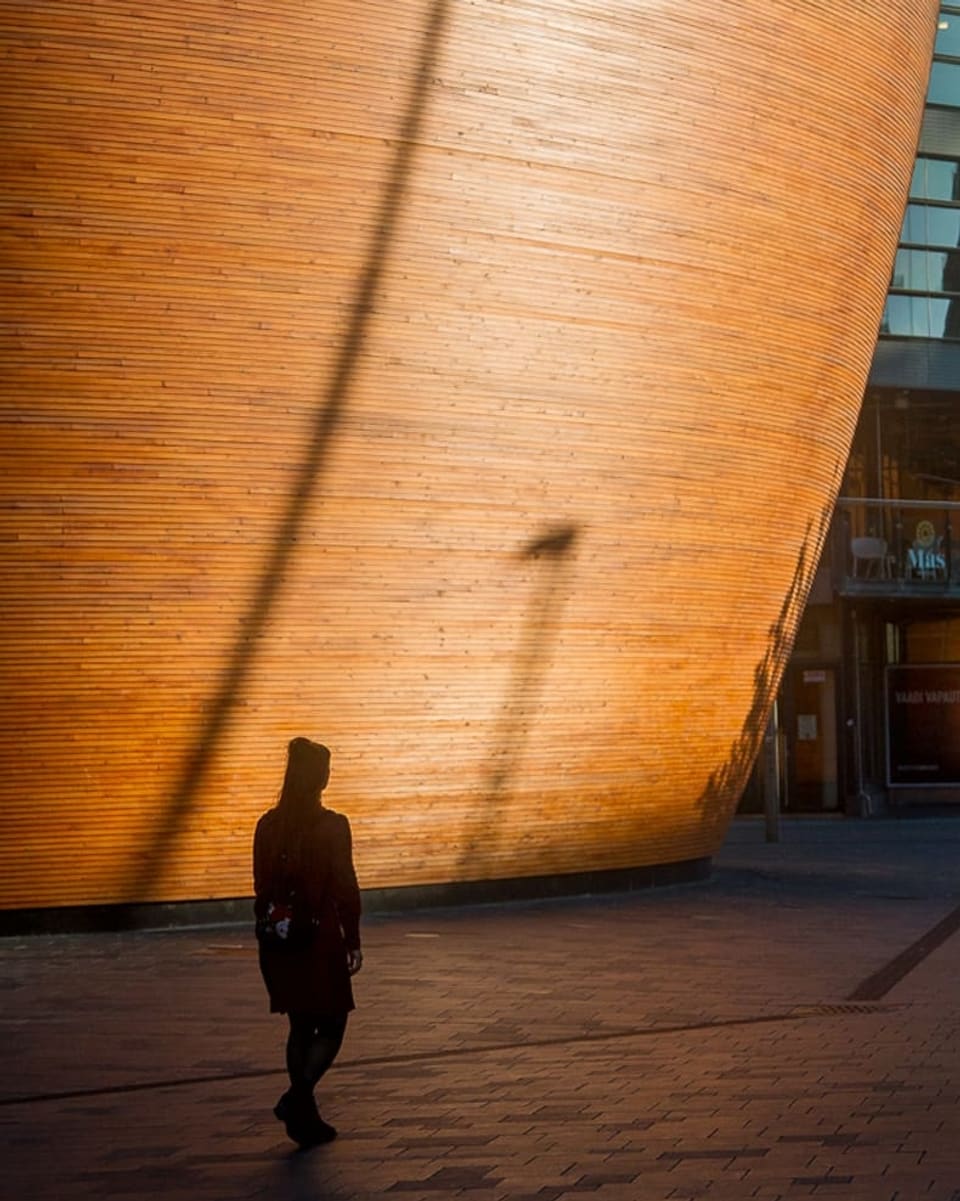 Eine Frau läuft bei Sonnenuntergang an einem Holzgebäude vorbei.