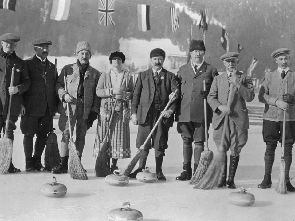 7 Männer und eine Frau posieren mit Curling-Steinen und Besen für die Kamera.