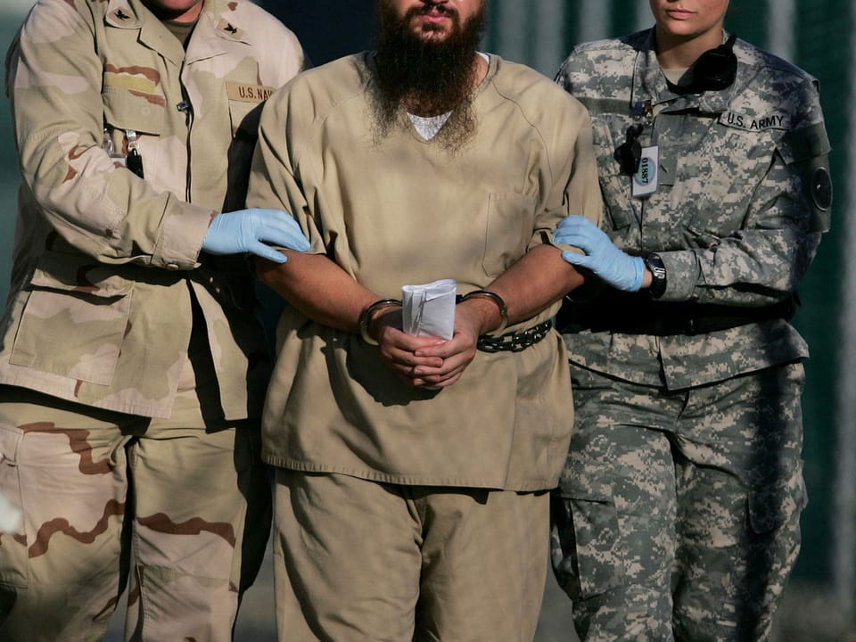 Zwei Armeeangehörige führen einen mit Handschellen gefesselten Guantanamo-Häftling ab.