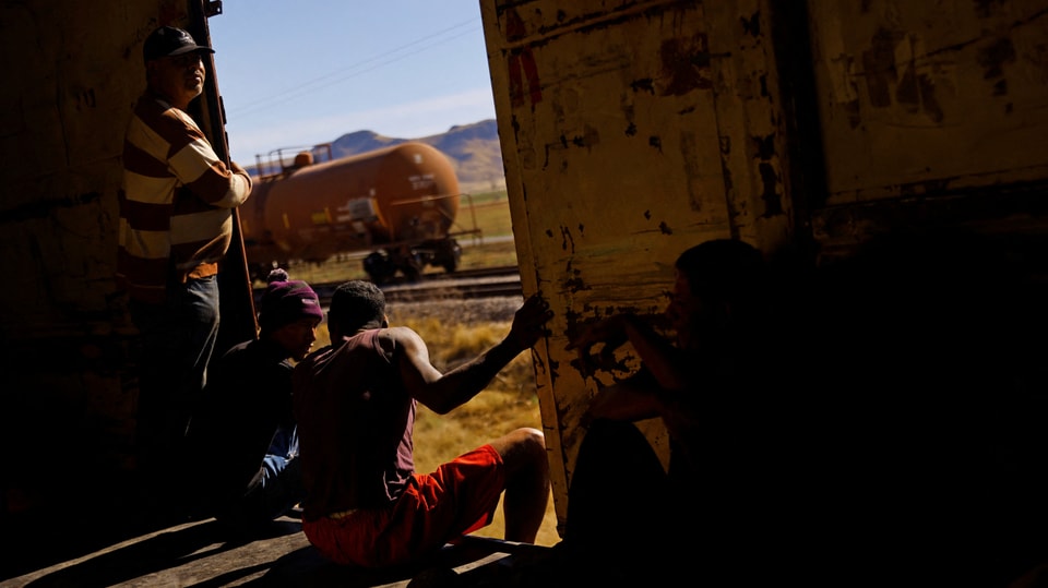 Migranten im Güterwagon bei Sonnenschein draussen.