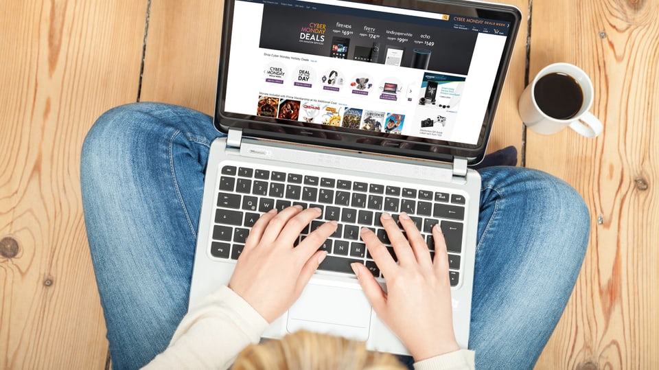 Symbolbild: Eine Person sitzt am Boden, einen Laptop auf dem Beinen, die Hände an der Tastatur, aufgerufen eine Website.
