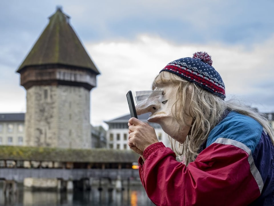 Eine verkleidete Person mit einer Maske steht vor dem Wasserturm in Luzern. Er fixiert mit seinem Blick das Handy.