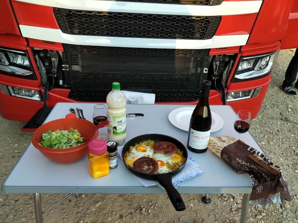 Piknik-Tisch mit einem Abendessen auf dem Tisch vor der Kühlerhaube eines LKW.