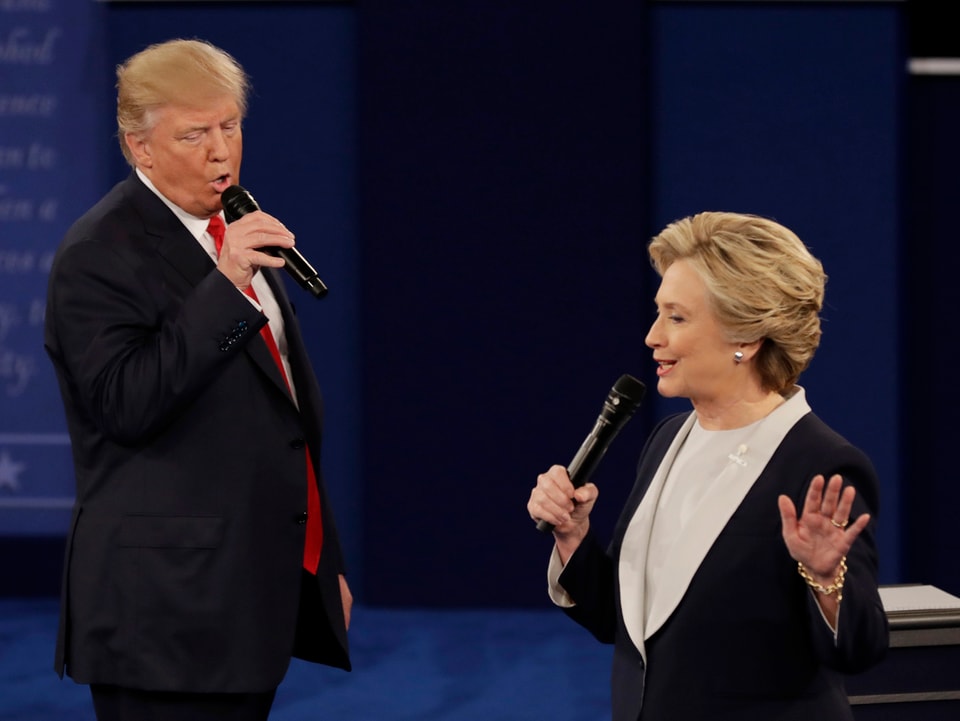 Trump und Clinton stehen sich gegenüber, beide sprechen – offenbar gleichzeitig – jeweils ins Mikrofon in ihrer Hand.