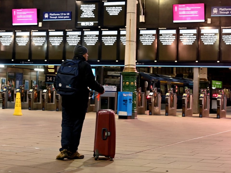Eine Person schaut auf die Informationstafeln welche die Zugausfälle verkünden in einem Bahnhof in Edinborough.